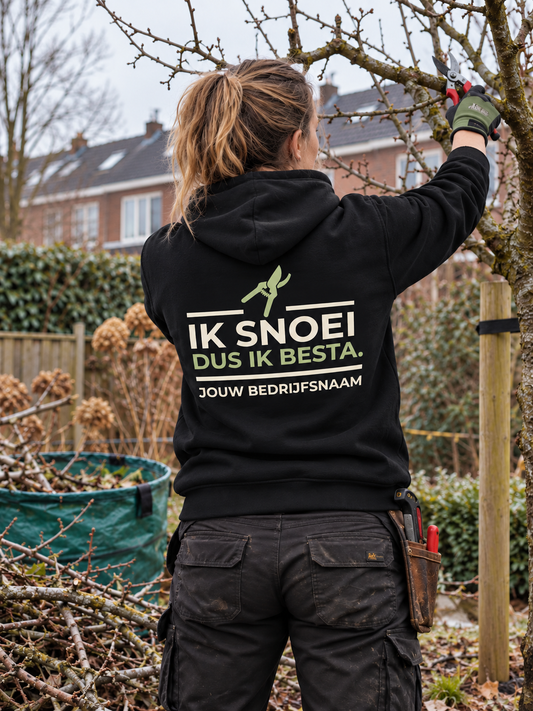 Hovenier in zwarte hoodie met de tekst "Ik snoei, dus ik besta" en bedrijfsnaam op de rug, snoeit een fruitboom in de winter